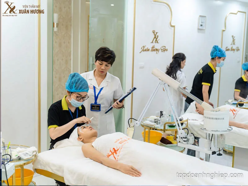 Instructor with a clipboard evaluating a student practicing facial skincare at Xuan Huong Beauty Institute