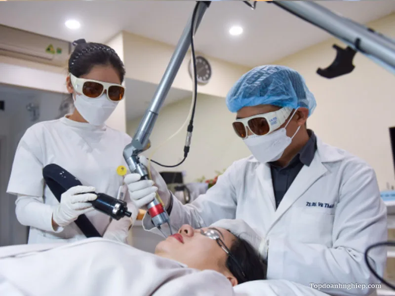 Bác sĩ da liễu và trợ lý đeo kính bảo hộ laser cẩn thận thực hiện quy trình bắn laser điều trị sắc tố môi và da mặt
