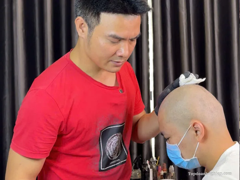 Close-up of an artist performing dotwork on a client's shaved head on a banner exploring the Best Scalp Micropigmentation Training in Hanoi