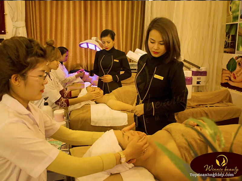 Instructors in black uniforms guiding students practicing facial and scalp aesthetics in a beauty academy classroom